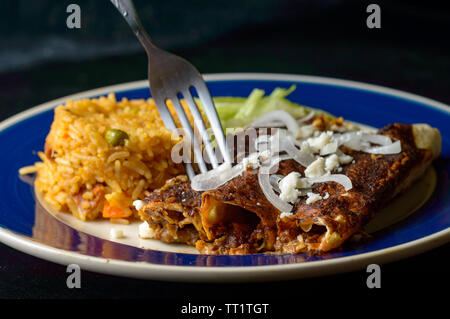 Mexikanische enmoladas, Enchiladas gekrönt mit Mole Sauce und Queso fresco, serviert mit Reis und Salat. Auf dunklem Hintergrund mit Kopie Raum isoliert Stockfoto