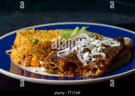 Mexikanische enmoladas, Enchiladas gekrönt mit Mole Sauce und Queso fresco, serviert mit Reis und Salat. Auf dunklem Hintergrund mit Kopie Raum isoliert Stockfoto