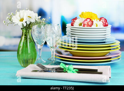 Stapel bunter Keramik Geschirr und Blumen, auf Holztisch, auf hellen Hintergrund Stockfoto