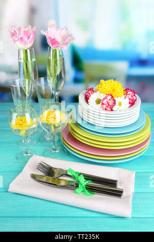 Stapel bunter Keramik Geschirr und Blumen, auf Holztisch, auf hellen Hintergrund Stockfoto