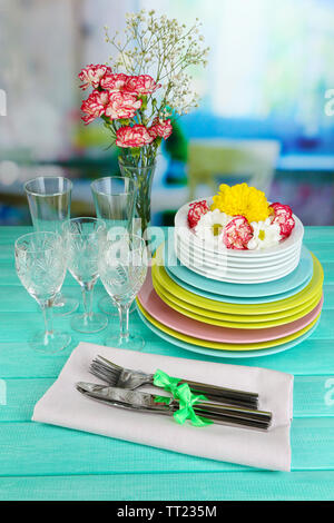 Stapel bunter Keramik Geschirr und Blumen, auf Holztisch, auf hellen Hintergrund Stockfoto