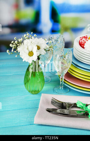 Stapel bunter Keramik Geschirr und Blumen, auf Holztisch, auf hellen Hintergrund Stockfoto