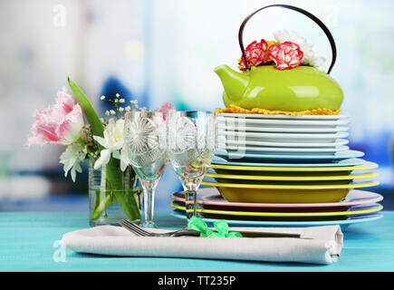 Stapel bunter Keramik Geschirr und Blumen, auf Holztisch, auf hellen Hintergrund Stockfoto