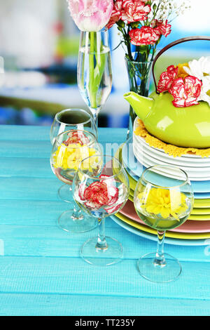 Stapel bunter Keramik Geschirr und Blumen, auf Holztisch, auf hellen Hintergrund Stockfoto