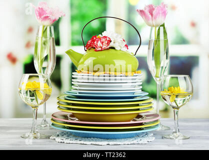 Stapel bunter Keramik Geschirr und Blumen, auf Holztisch, auf hellen Hintergrund Stockfoto