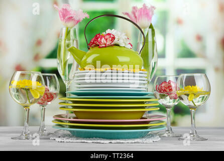 Stapel bunter Keramik Geschirr und Blumen, auf Holztisch, auf hellen Hintergrund Stockfoto