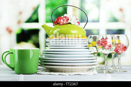 Stapel bunter Keramik Geschirr und Blumen, auf Holztisch, auf hellen Hintergrund Stockfoto