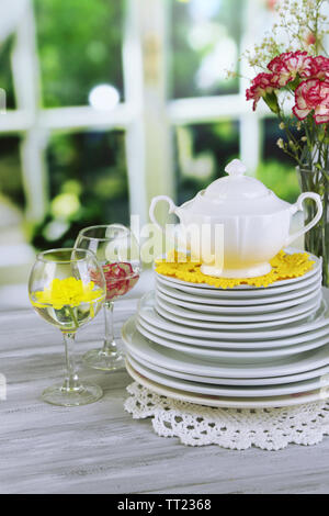Stapel bunter Keramik Geschirr und Blumen, auf Holztisch, auf hellen Hintergrund Stockfoto