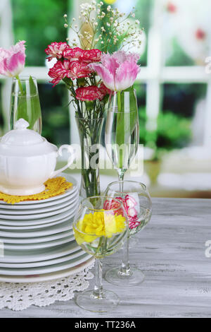 Stapel bunter Keramik Geschirr und Blumen, auf Holztisch, auf hellen Hintergrund Stockfoto