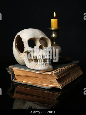 Schädel und Kerze auf altes Buch isoliert auf Schwarz Stockfoto