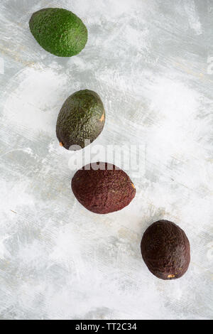 Vier Avocados in Phasen der Reifung auf rustikalen Holzmöbeln Hintergrund in Flach Komposition. Vertikales Format mit Platz für Text. Gesunde Ernährung Konzept. Stockfoto