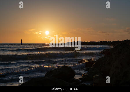 Sonnenuntergang Himmel am Jetty wie Wellen über die Felsen Stockfoto