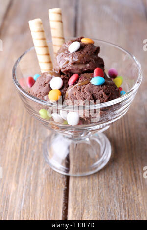 Schokoladeneis mit bunten Bonbons und Waffelröllchen in Glas Schüssel, auf Holz- Hintergrund Stockfoto