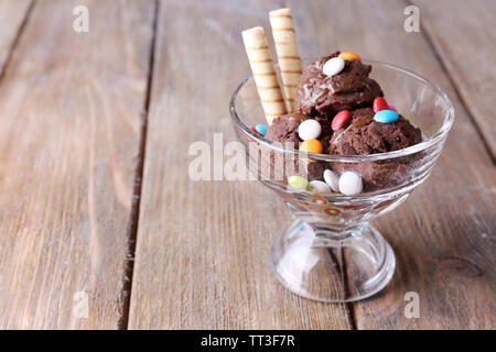 Schokoladeneis mit bunten Bonbons und Waffelröllchen in Glas Schüssel, auf Holz- Hintergrund Stockfoto