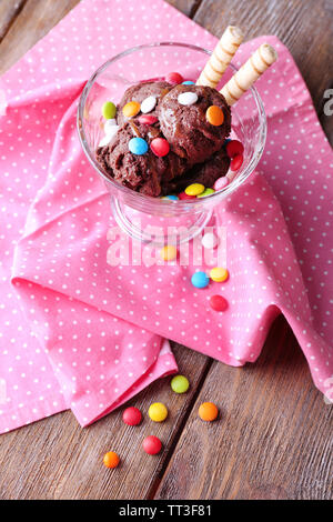 Schokoladeneis mit bunten Bonbons und Waffelröllchen in Glas Schüssel, auf Holz- Hintergrund Stockfoto