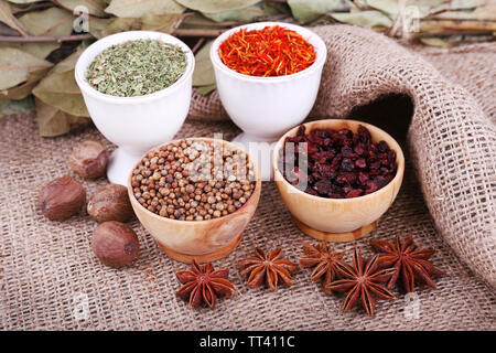 Kleine runde Kaffee und Hölzerne Schüsseln mit verschiedenen Gewürzen und Bay Blätter und Samen auf ein Stück Sackleinen closeup Stockfoto