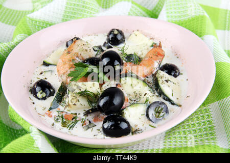 Frische Garnelen mit Oliven, Avocado und Petersilie in weißer Soße auf Rosa runde Platte auf grün Serviette closeup Stockfoto