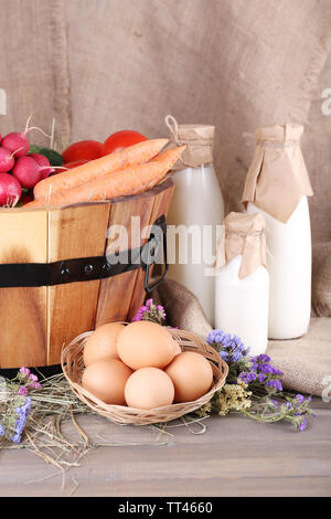 Großer runder Korb mit getrocknetem Gras, Gemüse, Milch und frischen Eiern auf plünderungen Hintergrund Stockfoto