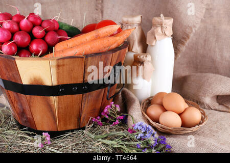 Großer runder Korb mit getrocknetem Gras, Gemüse, Milch und frischen Eiern auf plünderungen Hintergrund Stockfoto