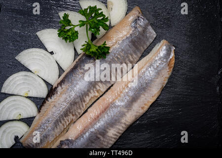 Leckere gesalzene Heringe, garniert mit Gelbe Zwiebel und frischer Petersilie. Natürliche schwarze Stein. Clupea harengus festgelegt. Stockfoto