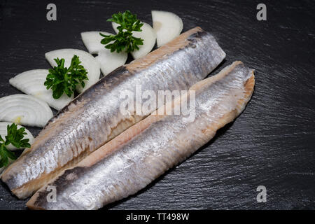 Leckere gesalzene Heringe, garniert mit Gelbe Zwiebel und frischer Petersilie. Natürliche schwarze Stein. Clupea harengus festgelegt. Stockfoto