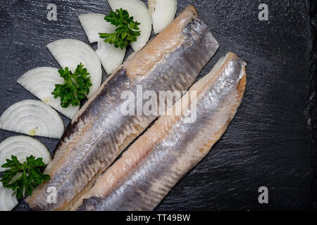 Leckere gesalzene Heringe, garniert mit Gelbe Zwiebel und frischer Petersilie. Natürliche schwarze Stein. Clupea harengus festgelegt. Stockfoto