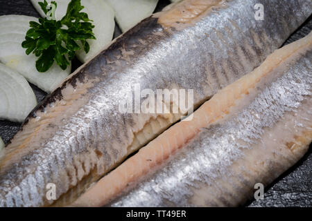 Leckere gesalzene Heringe, garniert mit Gelbe Zwiebel und frischer Petersilie. Natürliche schwarze Stein. Clupea harengus festgelegt. Stockfoto