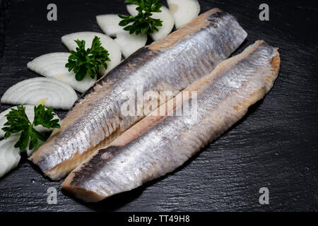 Leckere gesalzene Heringe, garniert mit Gelbe Zwiebel und frischer Petersilie. Natürliche schwarze Stein. Clupea harengus festgelegt. Stockfoto