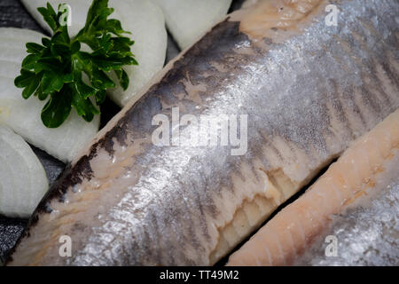 Leckere gesalzene Heringe, garniert mit Gelbe Zwiebel und frischer Petersilie. Natürliche schwarze Stein. Clupea harengus festgelegt. Stockfoto