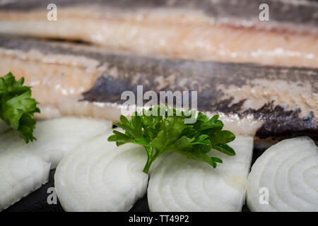 Leckere gesalzene Heringe, garniert mit Gelbe Zwiebel und frischer Petersilie. Natürliche schwarze Stein. Clupea harengus festgelegt. Stockfoto