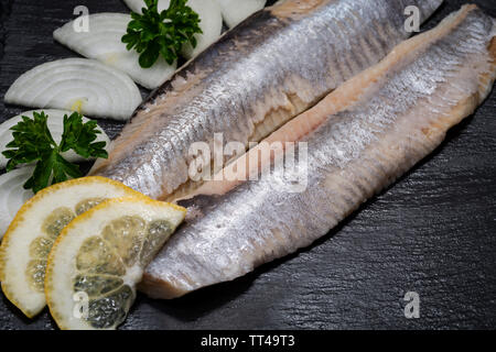 Gesalzene Heringsfilets ohne Knochen garniert mit Zitronenscheiben und frischer Petersilie. Natürliche schwarze Stein. Clupea harengus festgelegt. Stockfoto