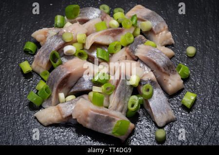 Schichten von gesalzenem Fleisch ohne Knochen, die in der Wildnis gefangen Atlantischer Hering garniert mit gehackten Frühlingszwiebeln Frühlingszwiebeln. Schwarz Naturstein Hintergrund. Clupea harengus festgelegt. Stockfoto