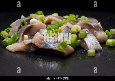 Schichten von gesalzenem Fleisch ohne Knochen, die in der Wildnis gefangen Atlantischer Hering garniert mit gehackten Frühlingszwiebeln Frühlingszwiebeln. Schwarz Naturstein Hintergrund. Clupea harengus festgelegt. Stockfoto