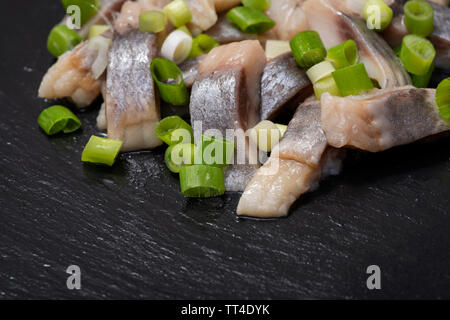 Schichten von gesalzenem Fleisch ohne Knochen, die in der Wildnis gefangen Atlantischer Hering garniert mit gehackten Frühlingszwiebeln Frühlingszwiebeln. Schwarz Naturstein Hintergrund. Clupea harengus festgelegt. Stockfoto