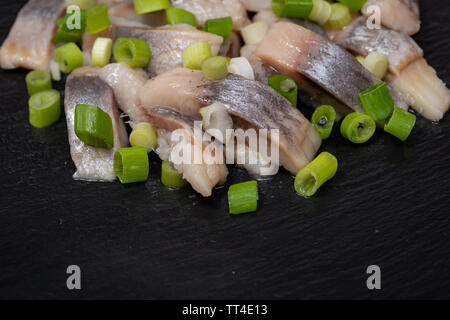 Schichten von gesalzenem Fleisch ohne Knochen, die in der Wildnis gefangen Atlantischer Hering garniert mit gehackten Frühlingszwiebeln Frühlingszwiebeln. Schwarz Naturstein Hintergrund. Clupea harengus festgelegt. Stockfoto