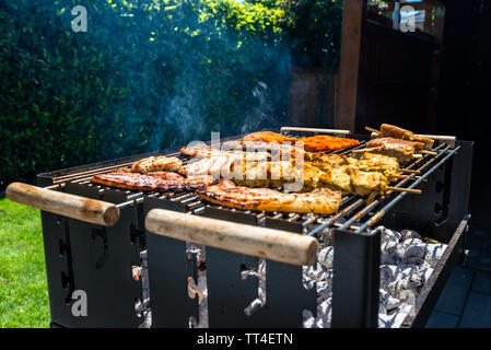 Verschiedene Arten von Fleisch gebraten auf der Startseite Grill, stehend auf einem Haus Garten auf den Pflasterstein. Stockfoto