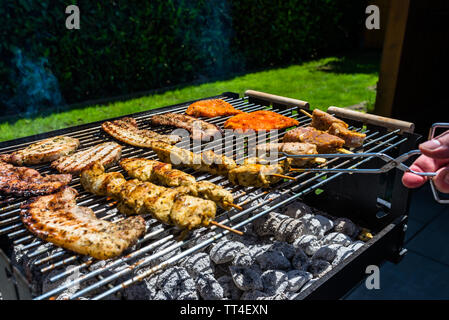 Verschiedene Arten von Fleisch gebraten auf der Startseite Grill, stehend auf einem Haus Garten auf den Pflasterstein. Stockfoto