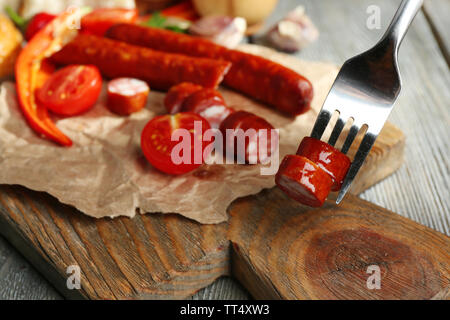 Dünne geräucherte Wurst und Gemüse auf ein Schneidbrett, auf hölzernen Hintergrund Stockfoto