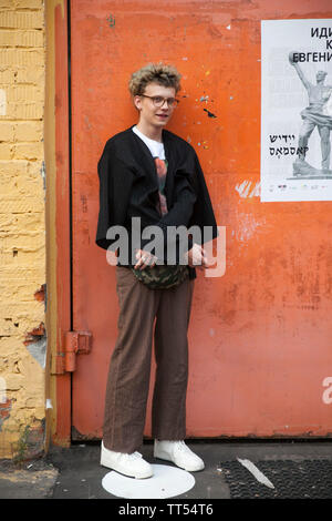 Moskau, Russland - Juni 12, 2019: Ein junger Mann in Beige weite Hose und einem schwarzen Orange Pullover in Gläser steht vor einem gelben Wand Stockfoto