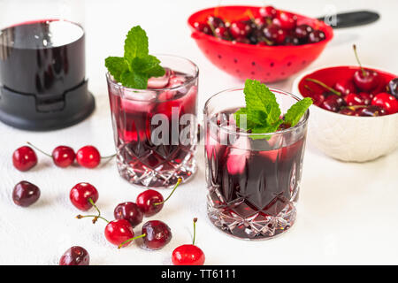 Frische kalte Cherry Saft in ein Glas mit Minze, Eis, Kirschen auf einem Küchentisch, Nahaufnahme auf weißem Hintergrund Stockfoto