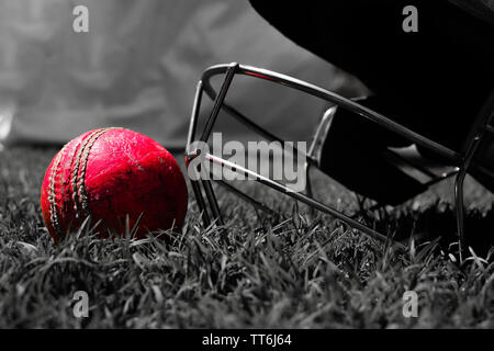 Rosa Cricket Ball mit Halmet auf grünem Gras. Schwarzweiß-Foto. Stockfoto
