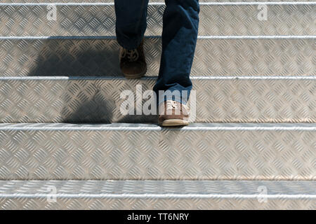 Beine einer Frau gekleidet in Jeans und tragen braune zeigt nach unten wandern helles Licht sauber Aluminium Treppenstufen Stockfoto