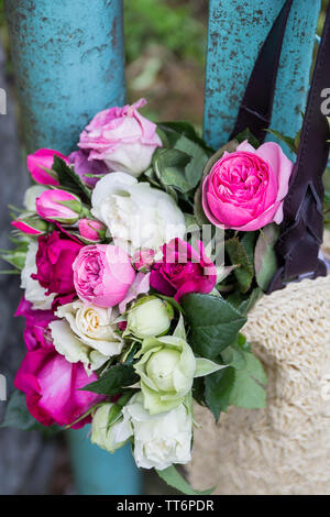 Blumenstrauß aus duftenden Englisch rosa und weißen Rosen in einer Tasche aus Bast hängt am Zaun Stockfoto