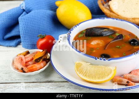 Lecker Suppe mit Garnelen, Muscheln, Tomaten und schwarzen Oliven in Schale auf Holz- Hintergrund Stockfoto