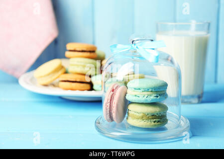Sanfte bunte Makronen in Glas Bell jar, Milch Glas und Handtuch auf Farbe holztisch Hintergrund Stockfoto