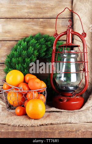 Petroleumlampe mit Kranz und Orangen in Weidenkorb auf Holzbohlen Hintergrund Stockfoto