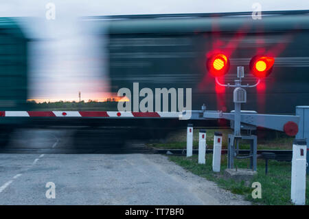 Zwei Ampeln mit rotem Licht und Barriere im Hintergrund bewegen Wagen und Sonnenuntergang Stockfoto