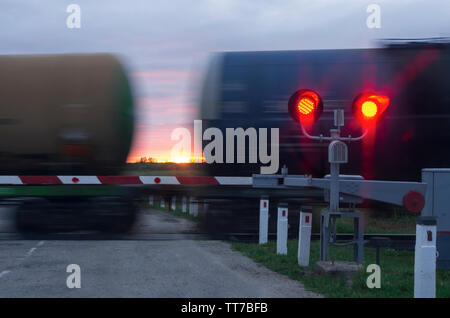 Zwei Ampeln mit rotem Licht und Barriere im Hintergrund bewegen Wagen und Sonnenuntergang Stockfoto