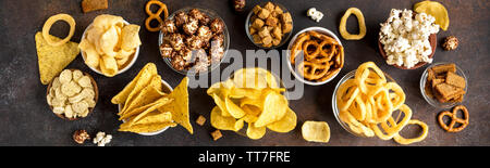 Sortiment von ungesunden Snacks: chips, Popcorn, nachos, Brezeln, Zwiebelringe in Schalen, Ansicht von oben, Banner. Ungesunde Konzept essen. Stockfoto