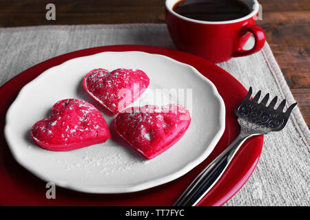 Cookies in Form von Herzen in der Platte mit Tasse Kaffee auf Serviette, auf rustikalen hölzernen Planken Hintergrund Stockfoto